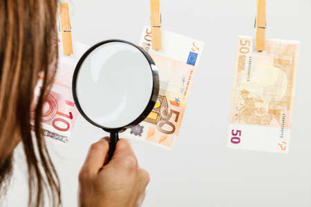 Currency exchange concept. Man worker check verify money cash. Payment hang on laundry line. Guy with loupe.の写真素材