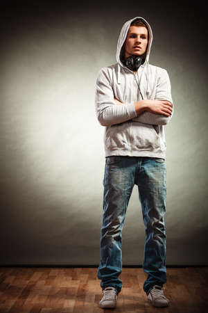 Full body young handsome man in hood with headphones listening to music dark grunge  backgroundの写真素材