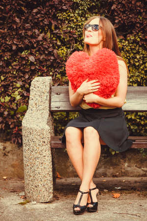 Love romance loneliness concept. Smiling girl sitting on bench. Cheerful lady with heart symbol.の写真素材