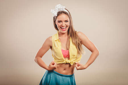 Happy strong pretty pin up girl with hairband bow showing off muscles. Young gorgeous retro woman in studio.の写真素材