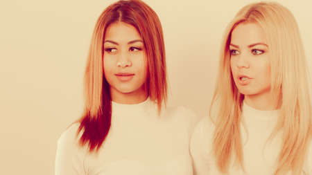 Friends people concept. Two young friends together. Girls have white top, standing next to each other. One lady has blonde hair, second dark ones.の写真素材