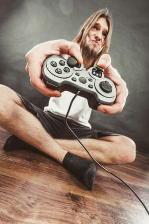 Addiction effects concept. Young unhappy depressed man with pad joystick playing games. Male addicted to console playstation videogames.の写真素材
