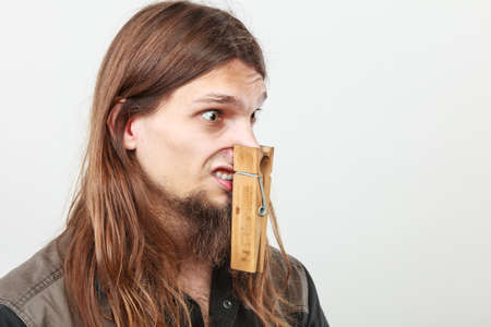 Unpleasant bad smell concept. Portrait of young long haired man with clogged nose by big clothespin.