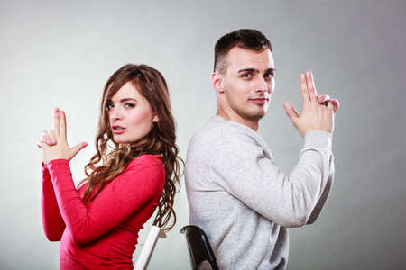 Happy couple having fun and fooling around pretending their hands fingers are guns. Joyful man and woman have nice time sitting back to back. Good relationship.の写真素材