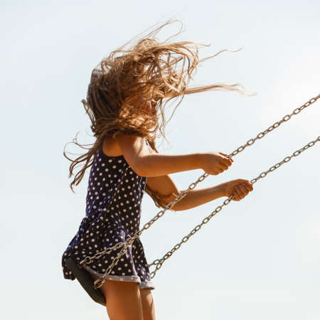 Craziness and freedom. Young summer girl playing on swing-set outdoor. Crazy playful child swinging very high to touch the sky.の写真素材
