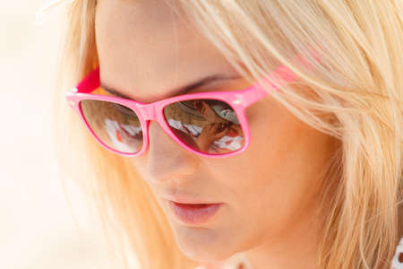 Young blonde pretty girl on beach. Woman wearing sunglasses have active time in summer. Summertime concept.の写真素材