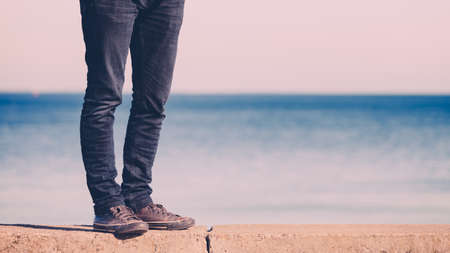 Male legs wearing denim trousers sneakers casual style walking relax by seaside at summer sunnyの写真素材