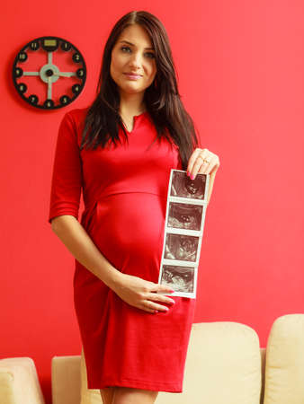 New life concept. Pregnancy, motherhood and happiness. Tummy of pregnant woman wearing elegant red...