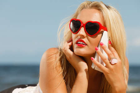 Young girl lying on beach with sunglasses talking using cellular phone. Communication and internet...