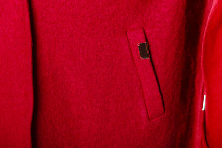 Closeup fragment of casual red coat with pocket and metal sign as background textureの写真素材