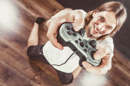Playing games. Young smiling cheerful man play on console . Guy with pad joystick.の写真素材