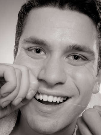 Daily health care. Young man cleaning flossing his white teeth with dental floss, black &white photoの写真素材