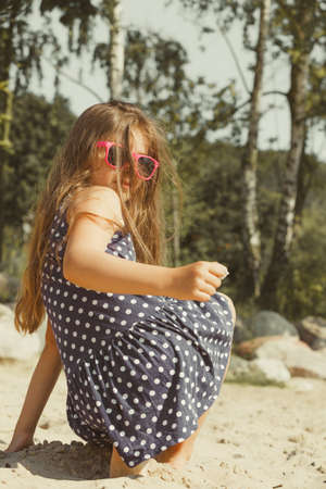 Having fun and joy concept. Little lovely gorgeous long haired girl playing with sea sand. Playful active kid on beach in summer vacation.の写真素材