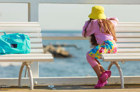 Summer holidays and leisure. Young little girl tourist in yellow cap outdoors. Child waiting for parent on seaside beach.の写真素材