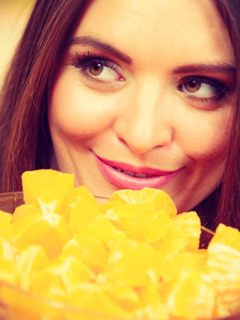 Woman young housewife in kitchen holds bowl full of sliced orange fruits preparing to make fresh juice or salad. Healthy eating, cooking, vegetarian food, dieting and people concept.の写真素材