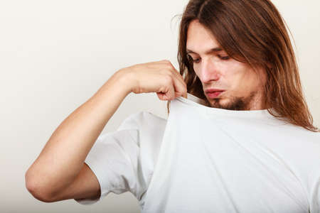 Expression of very bad smell. Young long haired sweaty man making hand gesture. Sweating concept.の写真素材