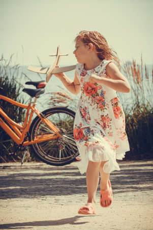 Little girl child kid having fun with cardboard paper plane airplane at beach. Summer vacation holiday relax and fun.の写真素材