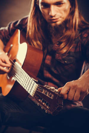 Music, hobby concept. Young guitarist is tuning guitar. Man is very focused and touching the...