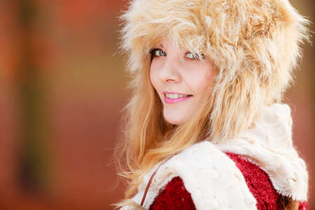 Portrait of pretty smiling fashionable woman in fall forest park. Happy gorgeous young girl in fur winter hat and sweater pullover. Autumn fashion.の写真素材