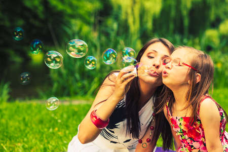 Mother and little girl daughter child blowing soap bubbles outdoor. Parent and kid having fun in...