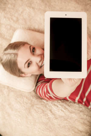 Woman laying and holding tablet computer with blank screen showing copyspace. Happy smiling woman advertising new modern technology.の写真素材