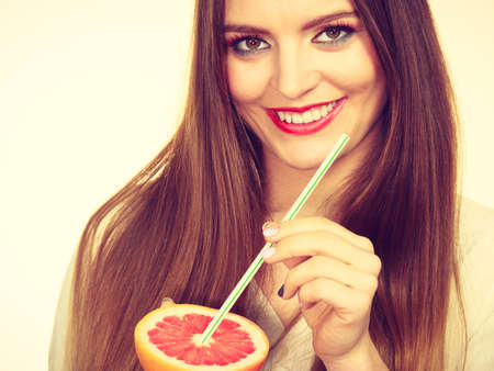 Woman attractive long hair girl eyes makeup holding grapefruit citrus sipping juice from fruit. Healthy diet food. Summer vacation holidays concept. Toned imageの写真素材