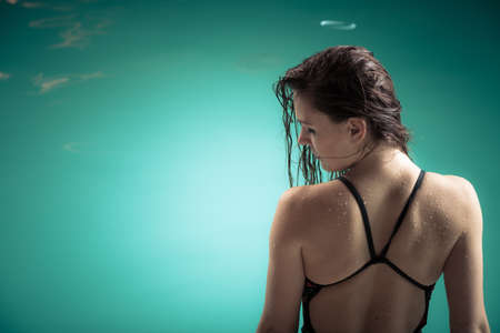 Exercising healthy lifestyle swimming sport. Young woman wear swimsuit sit at edge pool indoors.の写真素材
