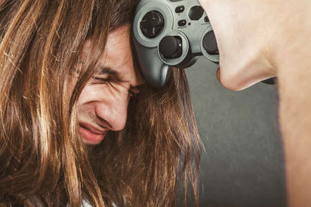 Addiction effects concept. Young unhappy depressed man with pad joystick playing games. Male addicted to console videogames.の写真素材