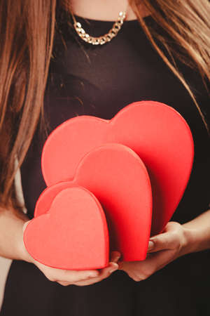 Valentine day. Woman in black holding three hearts boxes gifts presents. Part body of elegant model with valentines symbol sign. Studio shot.の写真素材
