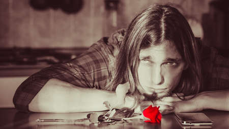 Disappointment and depression. Unrequited love concept. Young worried disappointed man with single red rose and smartphone mobile phone waiting for his girlfriend.の写真素材