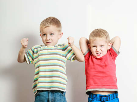 Free time, fun and independence. Little boys play together indoors make silly gestures emotions. Blonde siblings wear colorful clothes.の写真素材