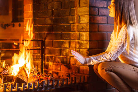 Woman warming hands up at fireplace. Young girl relaxing resting. Winter at home.の写真素材