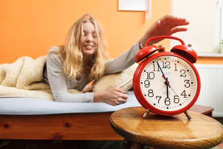 Woman waking up in bed turning off alarm clock. Young girl in the morning.の写真素材