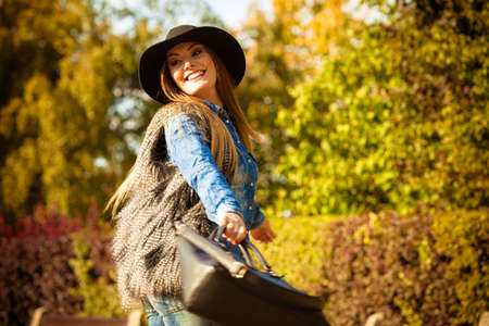 Beauty fashionable young woman having fun in park. Model wearing modern clothes in motion playing with her black bag outdoor.の写真素材