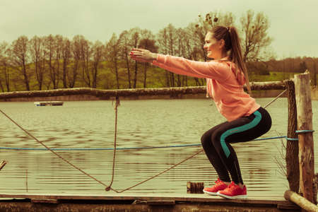 Sports and activities concept. Slim fit attractive woman exercising stretching outdoor. Young motivated girl training in sporty clothes on lake shoreの写真素材