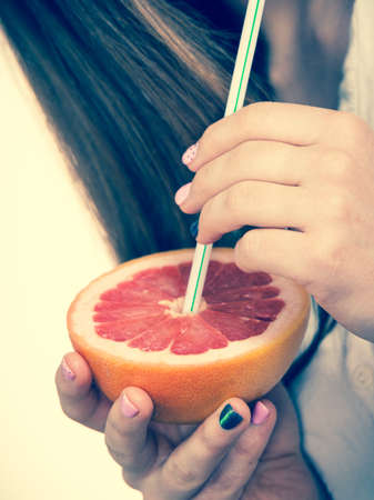 Woman holding grapefruit citrus sipping juice from fruit. Healthy diet food. Summer vacation holidays concept. Toned imageの写真素材