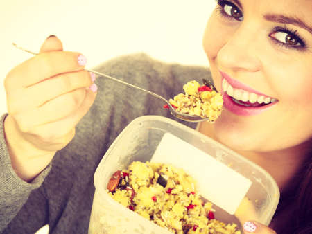 Woman eating oatmeal with nuts and dried fruits for breakfast. Girl holds plastic container take homemade lunch with healthy eating. Dieting nutrition conceptの写真素材