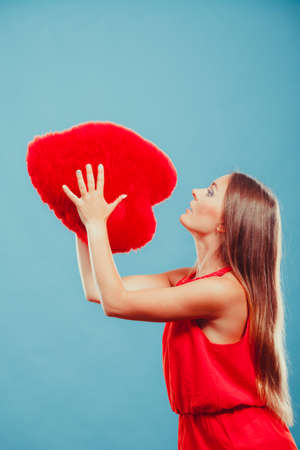 Pretty cute young woman girl throwing red heart shape pillow in studio on blue. Valentines day love.の写真素材