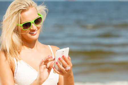Smiling young girl on beach with her mobile phone. Active relax using technology to be updated. Social network and internet concept.の写真素材