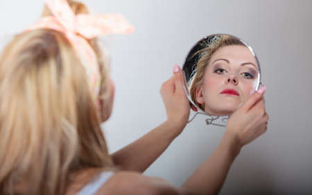 pin up beautiful blonde fashion girl in hairband looking at the mirror retro styling , studio shot gray backgroundの写真素材