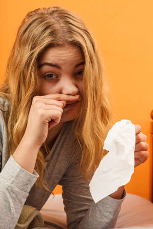 Sick woman laying in bed sneezing in tissue. Ill girl caught cold flu. Pills tablets and thermometer on table.の写真素材