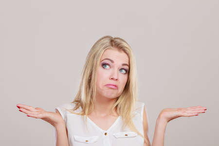 Shrugging woman in doubt doing shrug, attractive confused girl gesturing do not know sign on gray backgroundの写真素材