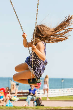Craziness and freedom. Young summer girl playing on swing-set outdoor. Crazy playful child swinging...