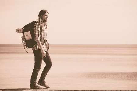 Man hiker backpacker walking with backpack by seaside at sunny day. Adventure, summer, tourism...