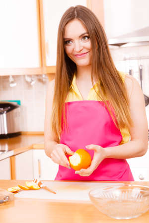 Woman young housewife in kitchen at home peeling orange fruit for salad or juicing. Healthy eating, cooking, raw food, dieting and people concept.の写真素材