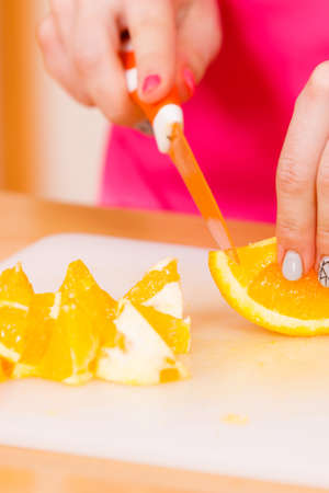 Woman young housewife in kitchen at home slicing fresh orange fruits on cutting board for salad or juicing. Healthy eating, cooking, raw food, dieting and people conceptの写真素材