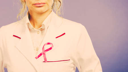 Awareness of breast cancer. Close up of white doctor medical uniform apron with pink ribbon symbol...