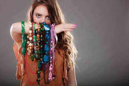 Pretty young woman wearing bracelets holding many plentiful of precious jewelry necklaces beads. Portrait of gorgeous fashion girl in studio on gray.の写真素材