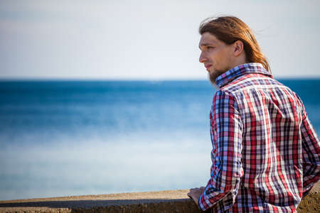Man bearded long hair wearing plaid shirt casual style relaxing by seaside at summer sunny windy dayの写真素材