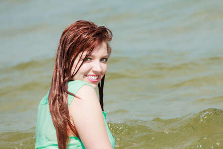 Vacation. Sensual girl wet cloth in water on the coast. Redhair woman having fun relaxing on the sea. Summertime.の写真素材